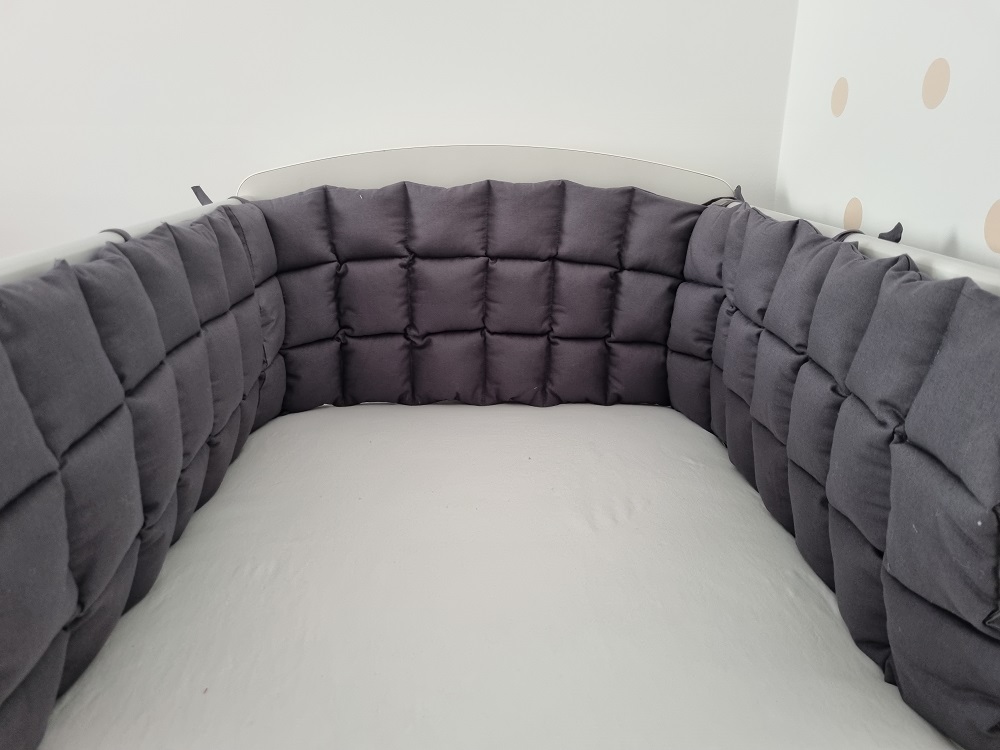 Sötétszürke steppelt rácsvédő kiságyban fényképezve