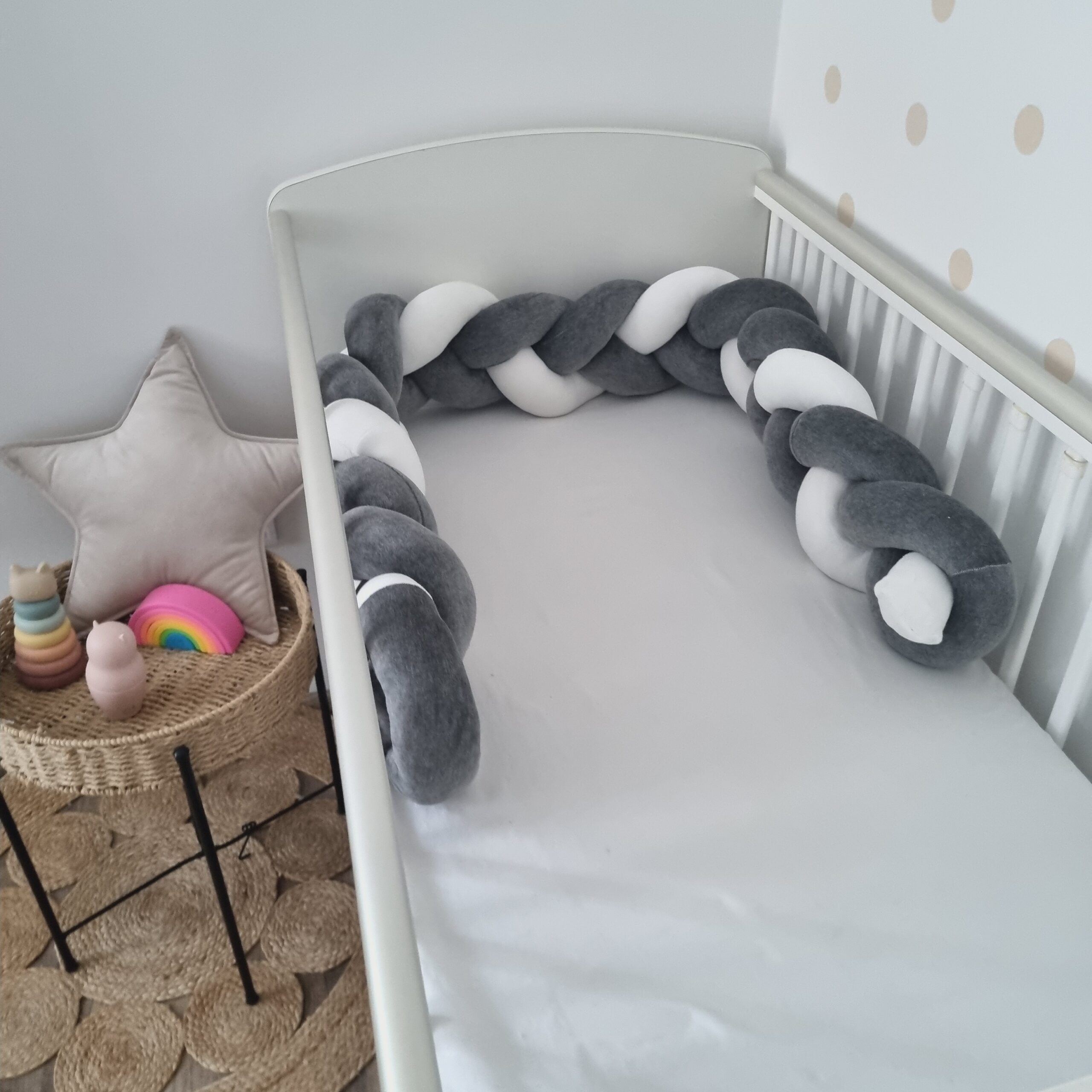 Fonott rácsvédő szürke fehér színben, babyplüss anyagból kiságyban oldalról fényképezve