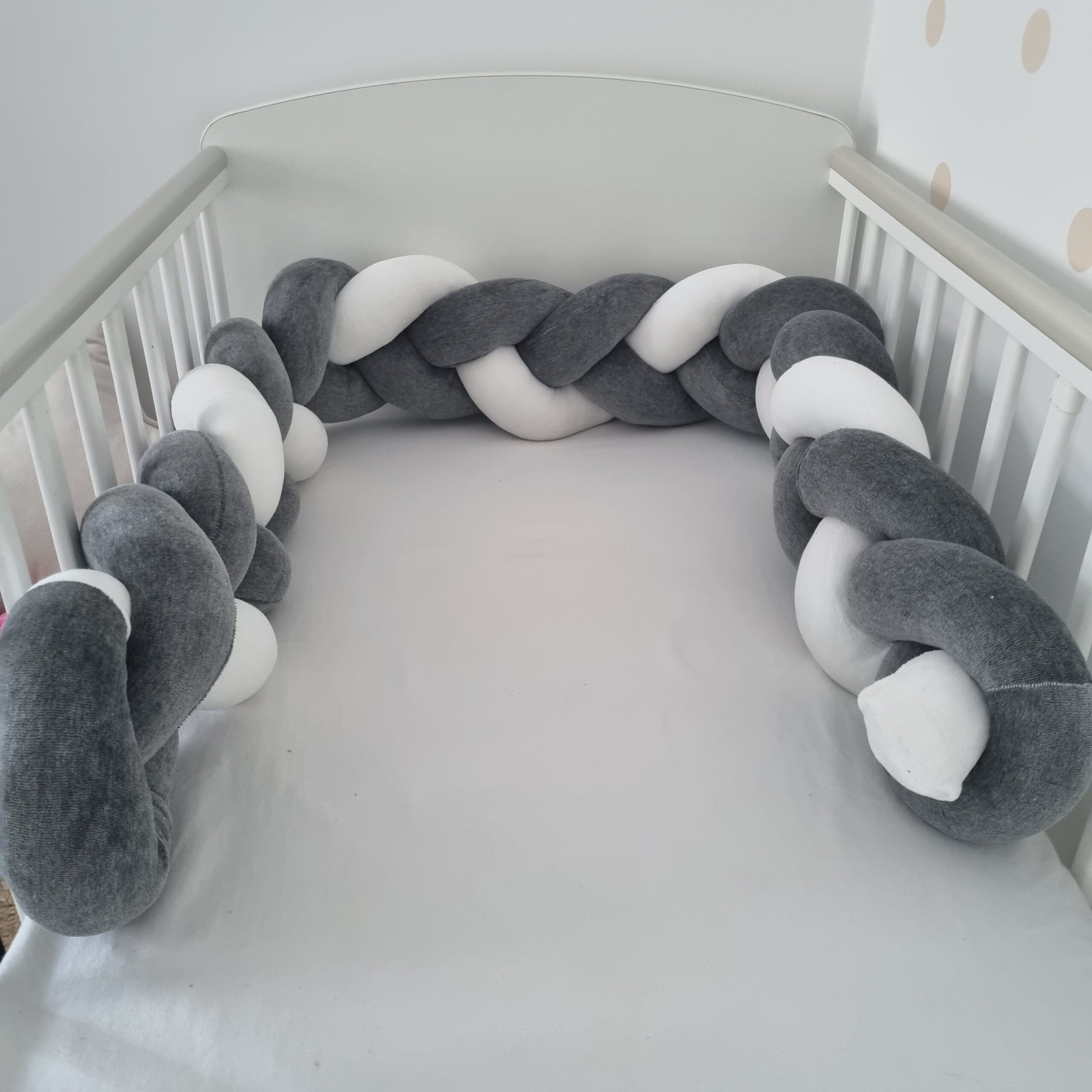 Fonott rácsvédő szürke fehér színben, babyplüss anyagból kiságyban fényképezve
