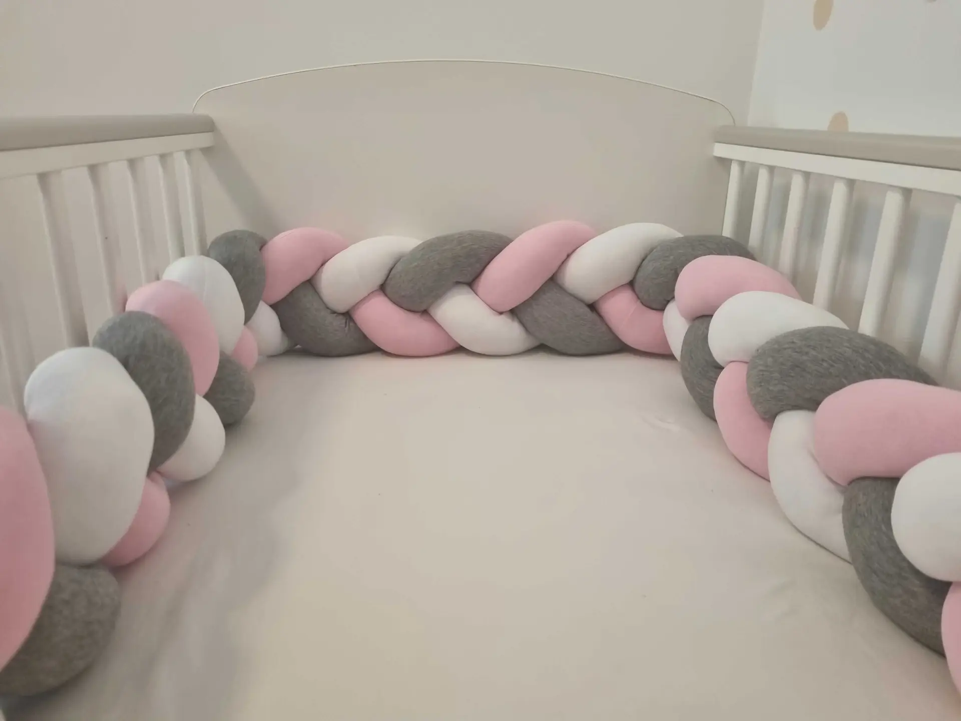 Fonott rácsvédő rózsaszín szürke fehér színben, babyplüss anyagból, babaágyban fényképezve méretben