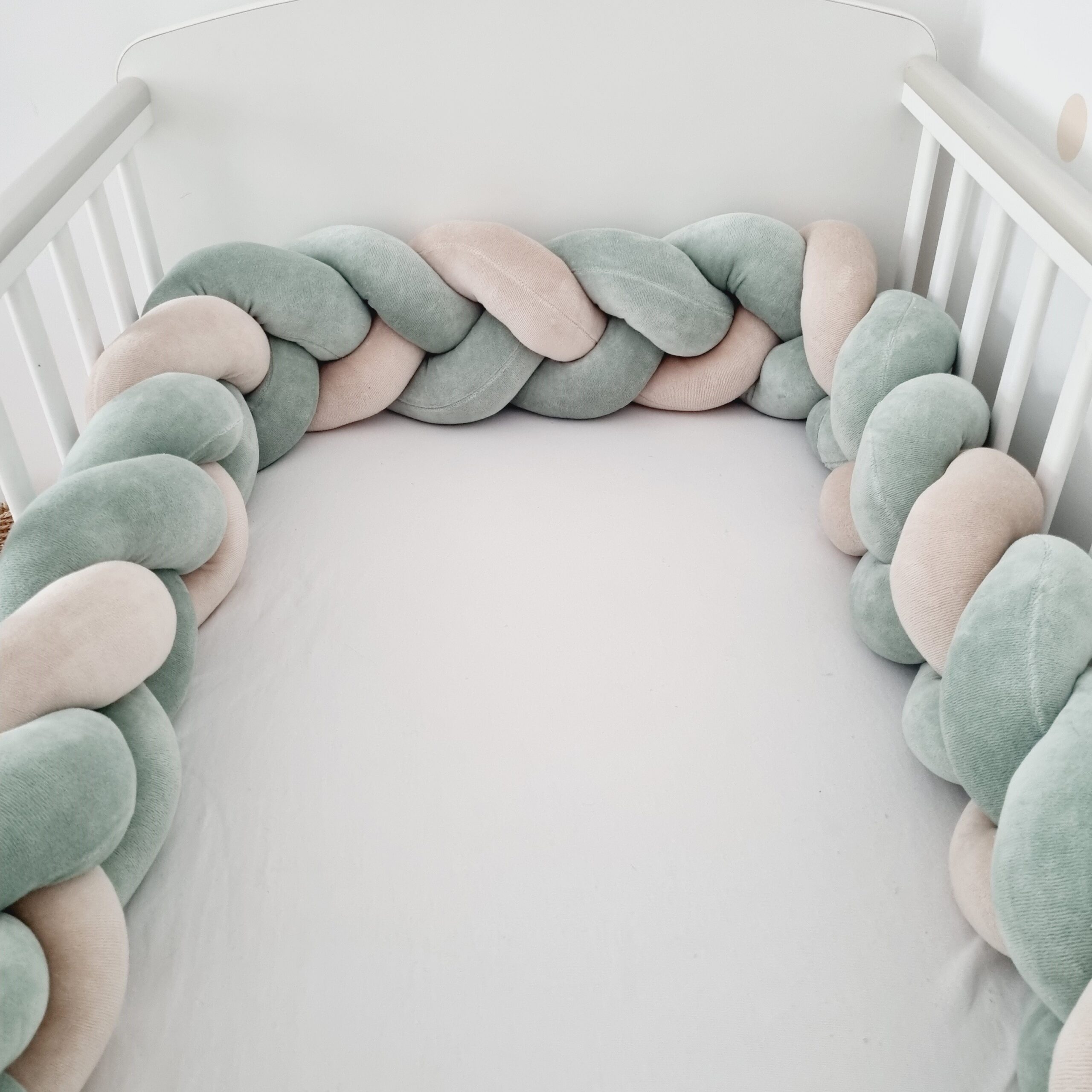 Közelről készült kép egy fonott babyplüss kiságy rácsvédőről zsálya és bézs színekben